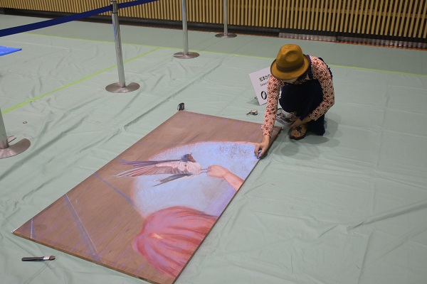 雨天のため中央体育館ワークショップスペースで板に絵を描く松本かなこさん